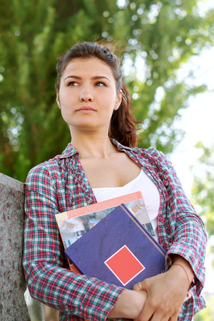 Girl student looks into the distance and keeps her books. Charming girl in a plaid shirt is thoughtの写真素材