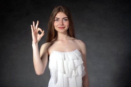 Confidence, happiness, satisfaction concept. Girl shows ok against a dark gray backgroundの写真素材