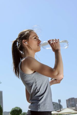 Woman is engaged in sports while listening to music. She is resting and drinking water.の写真素材