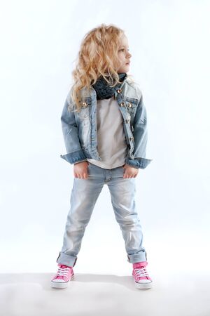 Little girl in denim suit and pink sneakers looking away with her hands in her pocketsの写真素材