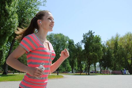 Sport woman running and listening to music with headphones in the phone outdoors against the skyの写真素材