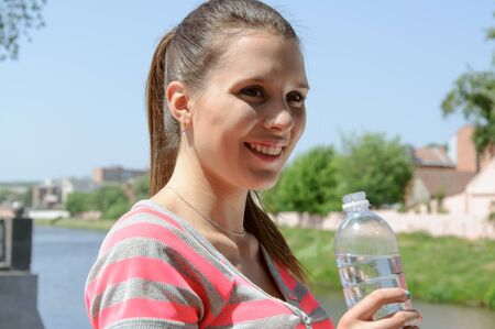 Sport woman drinking water and smiling against the waterfront outdoorsの写真素材