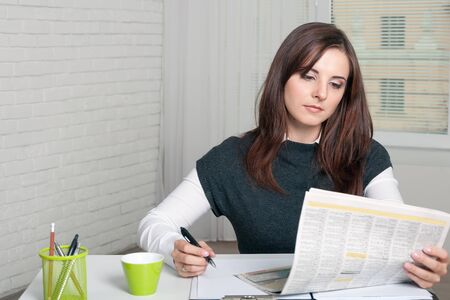 Secretary Girl reads a newspaper, making notes by a ballpoint penの写真素材
