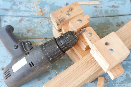 Old shabby screw gun lying on a wooden blocks