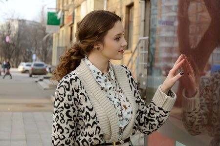 Photo in vintage style. The girl looks window of a shop on the background of the city.の写真素材