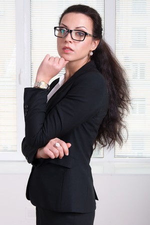 Woman leader in black business suit and glasses standing turned aside and propping up her hand chinの写真素材