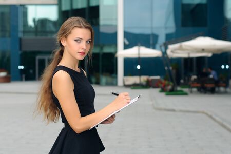 Business woman writing in a folder with documents and looking away against the background of the business centerの写真素材