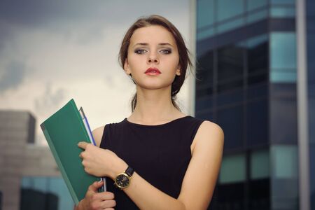 Business female in formal clothes goes on city's business district with folders for papers in her handsの写真素材