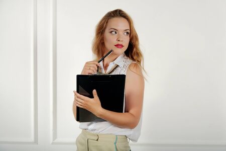 Girl with a folder in her hand looking away thoughtfully against a light backgroundの写真素材