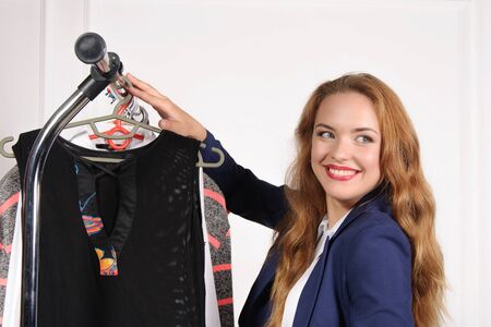 Woman in formal wear chooses black shirt in a clothing store and laughs against a light backgroundの写真素材