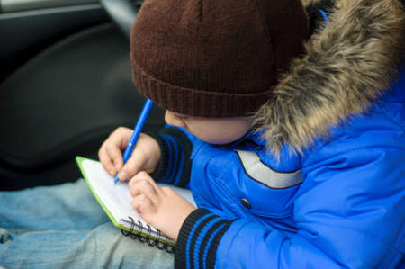 Boy writes in notebook sitting inside the car