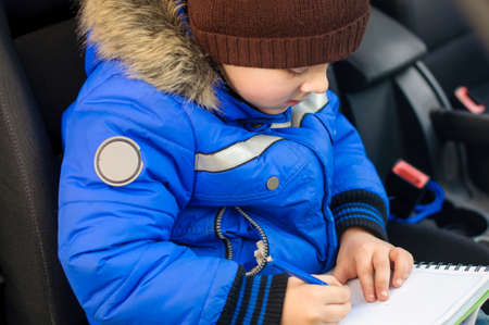 Young boy writes in notebook sitting inside the car