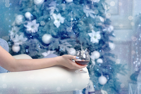 Woman sitting in a chair with a glass of cognac on the background of the Christmas treeの写真素材