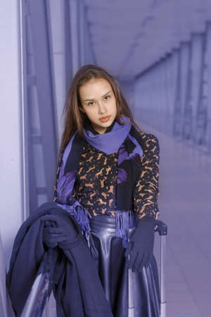 Girl standing with a suitcase and a coat in hand at the stationの写真素材