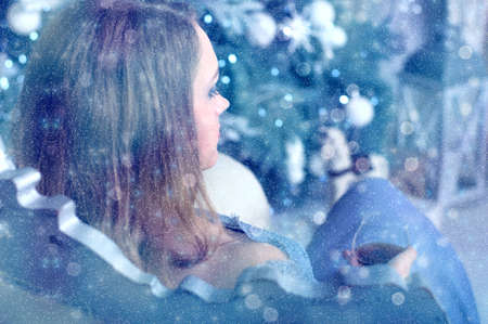 Girl sits in a chair with a glass of brandy in front of the Christmas treeの写真素材