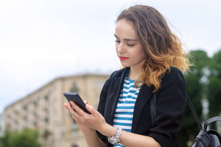 Woman communicates on a mobile phone and smiling at the background of the cityの写真素材