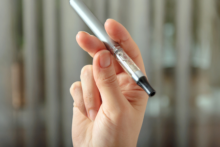 Electronic Cigarette in a female hand close up against the background blur. Concept: safe way of smoking, how to stop smokingの写真素材