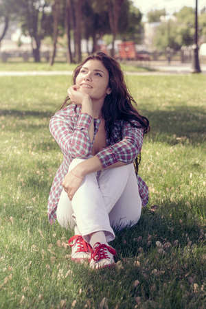 Student sitting in the park on the grass and looking up dreamily. Concept: study, college, exam, knowledgeの写真素材