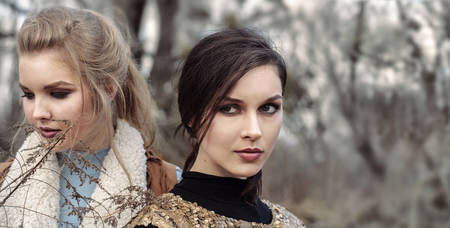 Two beautiful girls in fashionable dress posing against the backdrop of autumn forestの写真素材