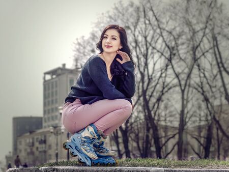 Girl in roller skates sitting against urban landscape. Concept: sports, lifestyle, health.の写真素材