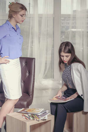 Two girls are looking for a solution and draw sketches with colored pencils in the office next to the window. Concept: creative, fashion, workの写真素材