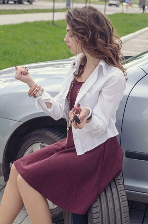 Woman paints her nails while sitting on a car tire next to her car