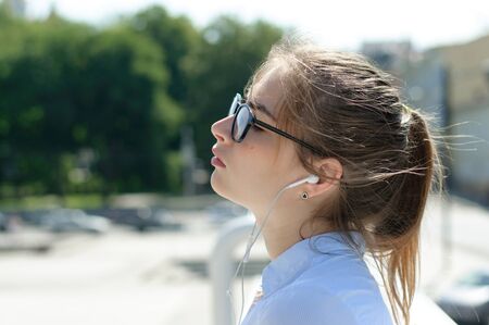 Girl listening to music through headphones on the background of the cityの写真素材