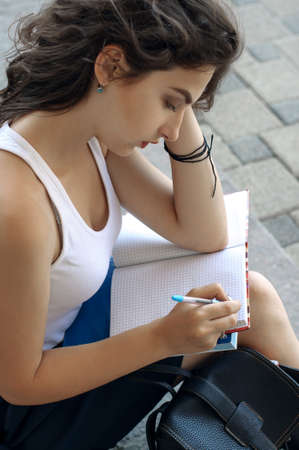 Girl with books sitting on the steps and writes in a notebook. Concept: study, education, knowledge