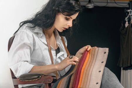 Fashion designer chooses the color and texture of fabric. She is dressed in a white shirt and she...