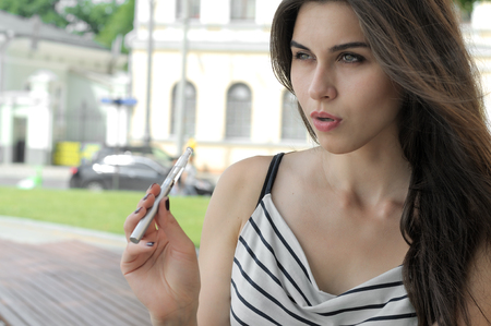 Beautiful woman smokes an electronic cigarette outdoors. She has perfect skin and wearing a striped t-shirt.の写真素材