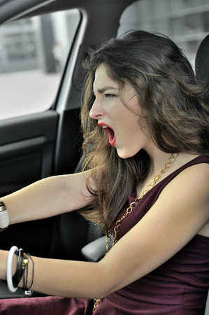 Girl shouts while sitting behind the wheel of a car. She has long hair and wearing a burgundy dressの写真素材
