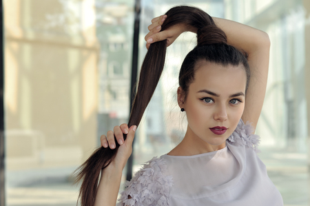 Portrait of a beautiful woman. She has long hair and well-groomed skin. Portrait on the background of modern architecture of metal and glass.の写真素材