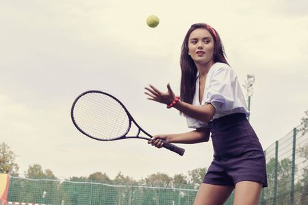 Girl playing tennis on green court. She is dressed in shorts and blouse against the background of the skyの写真素材
