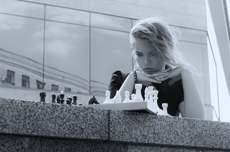 Portrait of a girl who looks at the chessboard with figures on it. Black and white photo in vintage style.の写真素材