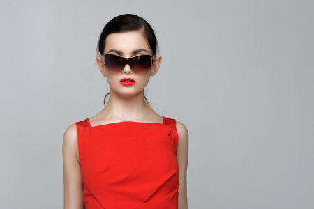 Beautiful girl with evening make-up in red dress and sunglasses against isolated background.の写真素材