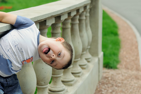 Boy shows tongue and hanging on the fence upside downの写真素材