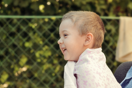 Cheerful little boy after a swim laughing wrapped in a towel outdoorsの写真素材