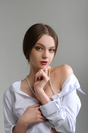 Girl takes off her clothes and bare her shoulders. She has a neatly arranged hair and bright make-up and she is wearing a white shirt.の写真素材