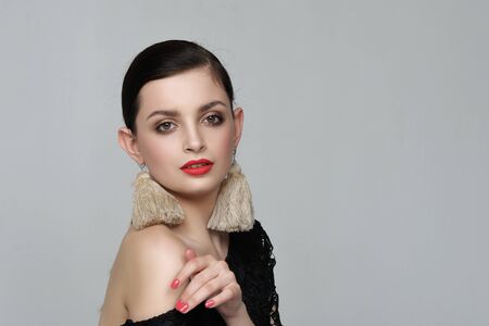 Portrait of a girl with self-made earrings made of string. She has hair tied in a ponytail and she is dressed in a black dress against a gray background in the studio.の写真素材