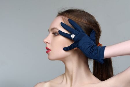 Close-up portrait of a beautiful girl who stands in profile with bare shoulders in a blue glove on her hand against an isolated backgroundの写真素材