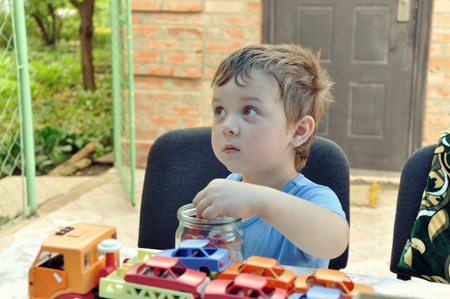 Little boy eating raspberries from glass jar sitting in the courtyard of his houseの写真素材