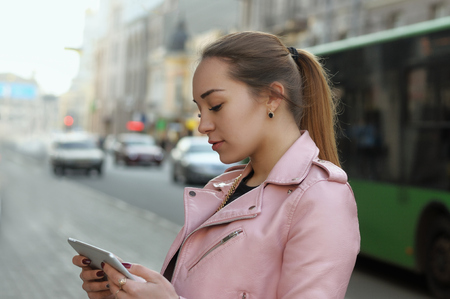 Girl uses the app on the tablet while walking through the streets of the city. Portrait on a background of city transport.の写真素材