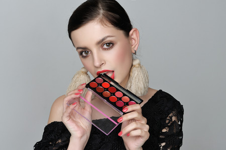 Beautiful girl holds a cosmetic palette of warm colors in her hands. She has evening make-up and perfect facial skin.の写真素材