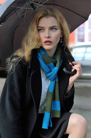 Portrait of a beautiful girl who stands under an umbrella during a rain on a city street backgroundの写真素材