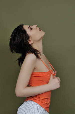 Beauty portrait of a girl in profile, who stretches the straps of her orange tank tops against a...