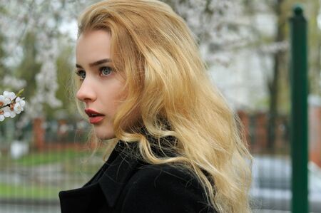 Close-up portrait of a girl with blond hair who walks along flowering apricot treesの写真素材