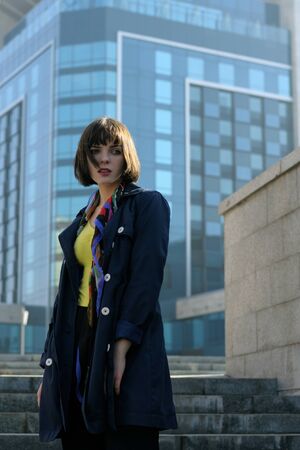 Business woman in formal clothes against the urban background. She has brown hair and a bob hairstyle, she is wearing a blue raincoat and a scarf around her neck.の写真素材