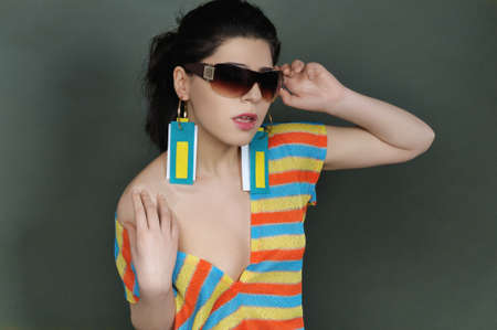 Portrait of a brunette in sunglasses and striped blouse. She bare her shoulder and in the girl's ears wear earrings in the form of tags of clothes.の写真素材