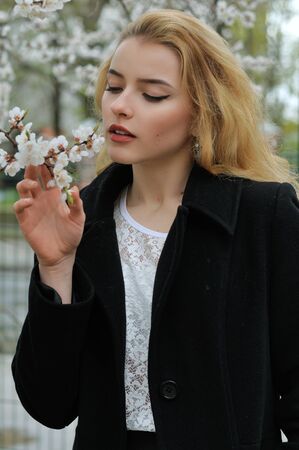 Girl enjoys the smell of flowering apricots while walking along the avenueの写真素材