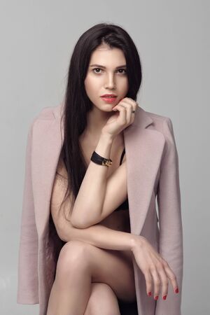 Girl in her underwear wore a coat over her naked body. She has daytime makeup, perfect skin, neat red nails and long dark hairの写真素材